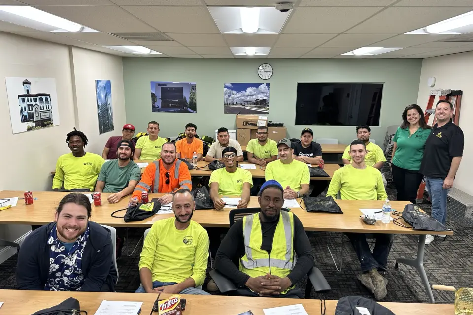 Tri-City Electrical Contractors A group of people are gathered in a classroom, sitting at tables and facing the camera. Some are wearing high-visibility vests and shirts.