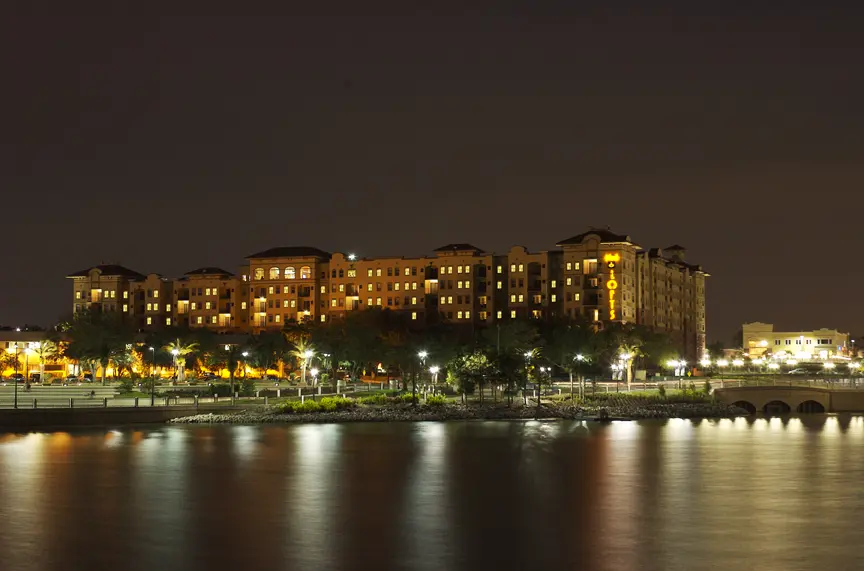 Tri-City Electrical Contractors The night view of The Lofts - Altamonte, a well-lit riverside hotel, casts a mesmerizing reflection on the calm water. Surrounded by trees and streetlights, the serene ambiance is perfectly complemented by a bridge visible on the right, capturing FLs tranquil essence.